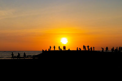 Silhouette people on beach against sky during sunset