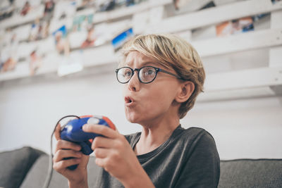 Boy playing video game while sitting on sofa in living room at home