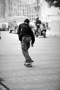 Rear view of men skating on street in city
