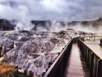 Pier by rocky mountains and geyser against sky