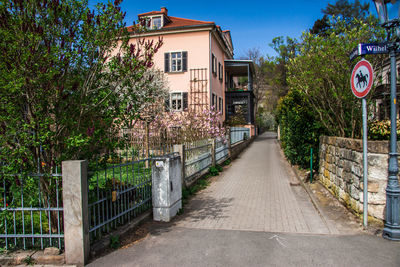 Footpath amidst trees and buildings against sky