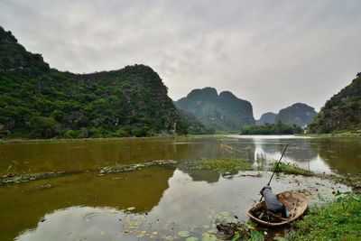 Rear view of man in boat on lake against sky