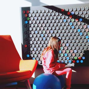 Side view of girl sitting on seat against wall at home