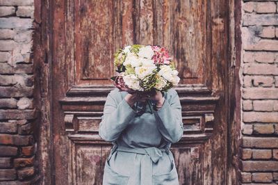 Woman with face covered by flowers against wooden door