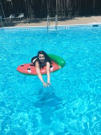 High angle portrait of young woman lying on inflatable raft in swimming pool