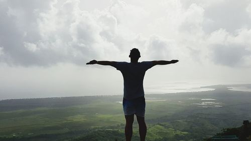 Rear view of man with arms outstretched standing on landscape