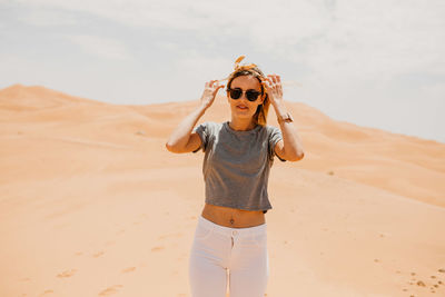 Young woman wearing sunglasses standing on sand dune