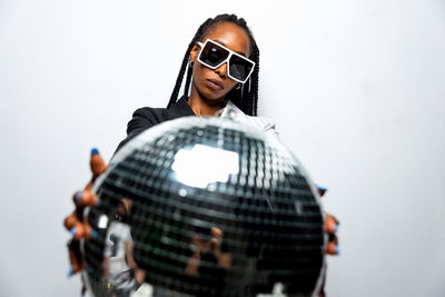 Portrait of young woman wearing sunglasses standing against white background