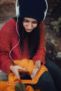 High angle view of young woman wearing sweater listening music sitting in forest