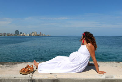 Woman sitting on beach by sea against sky