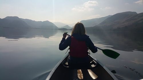 Rear view of woman canoeing in lake by mountains against sky