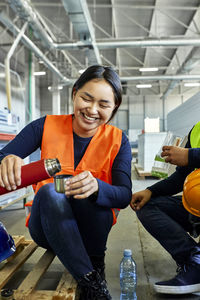 Happy female worker pouring drink into mug during lunch break in factory