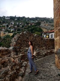 Full length of young woman standing on footpath against buildings in city