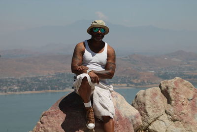 Portrait of man sitting on rock against lake