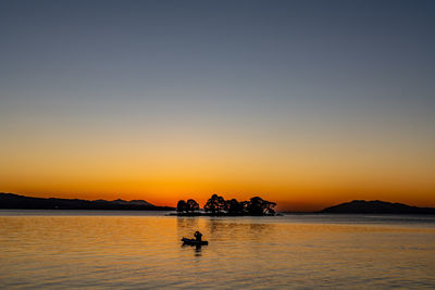 Silhouette people on sea against clear sky during sunset