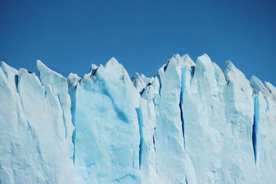 Low angle view of glacier against clear blue sky