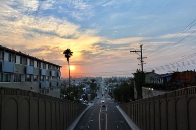 Road amidst buildings in city against sky during sunset