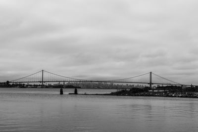 View of suspension bridge over river against cloudy sky