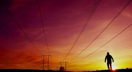 Silhouette of electricity pylon against sky during sunset