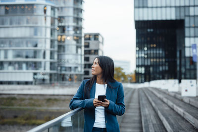 Thoughtful businesswoman standing near railing in front of buildings