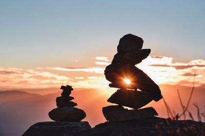 Close-up of silhouette stacked pebbles rocks on field against orange sky