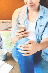 Cropped image of woman using smart phone while sitting at home