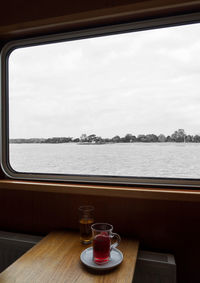 Glass of table by sea against sky seen through window