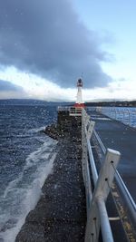 Scenic view of ocean lighthouse on pier with sea spray action. 