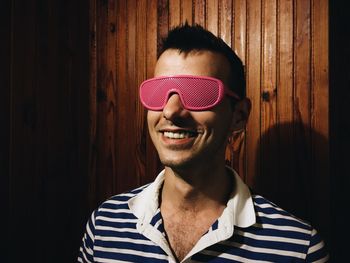 Smiling young man wearing eyeglasses against wooden wall
