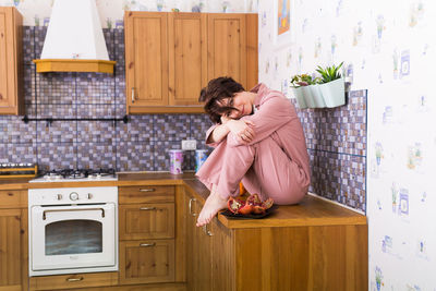 Full length of woman sitting on kitchen at home