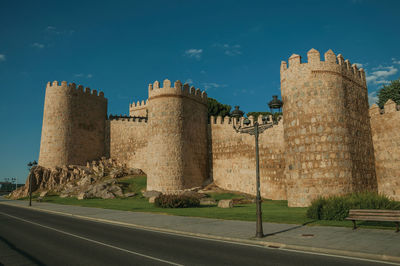 Street and light posts beside stone towers in the large wall encircling the town of avila, in spain.