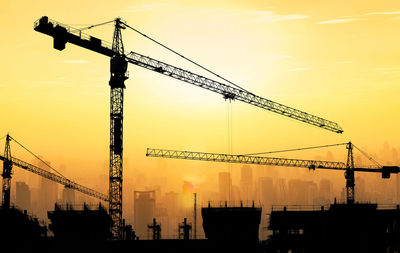 Low angle view of silhouette cranes against sky during sunset