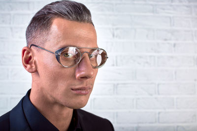 Close-up portrait of man wearing eyeglasses against wall