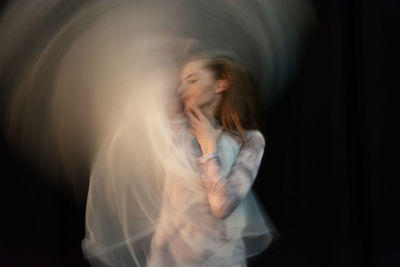 Blurred motion of woman dancing against black background