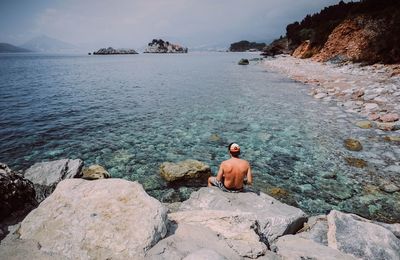 Rear view of man sitting on rock by sea