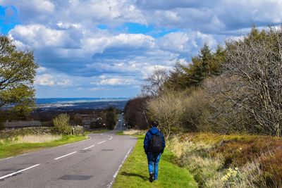 Rear view of man walking on road against sky