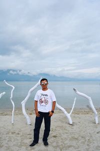 Full length portrait of young man standing at beach against sky