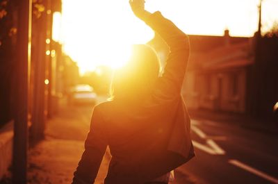 Rear view of girl dancing amidst buildings during sunset