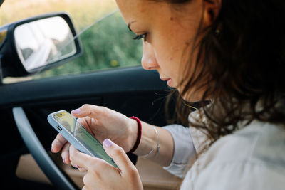 Close-up of young woman using mobile phone in car