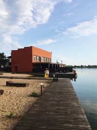 Pier over lake by buildings against sky