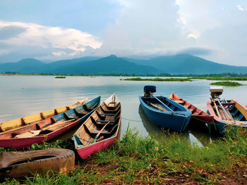 Boats moored on shore by lake against sky