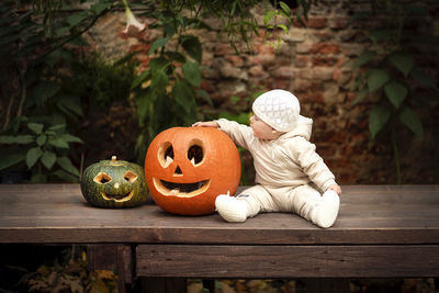 Baby sitting by jack o lantern on wooden table