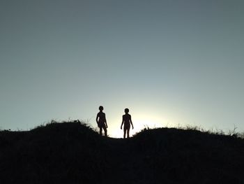 Low angle view of silhouette girls standing on field against clear sky during sunset