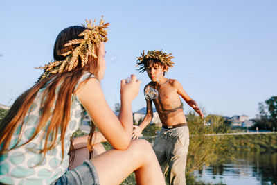 Boy and girl playing with bubbles by lake against sky