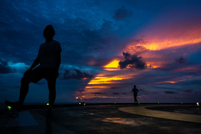 Silhouette people standing by sea against sky during sunset