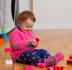 Cute girl playing with toy sitting on wooden floor