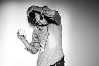 Young man with tea cup standing against white background