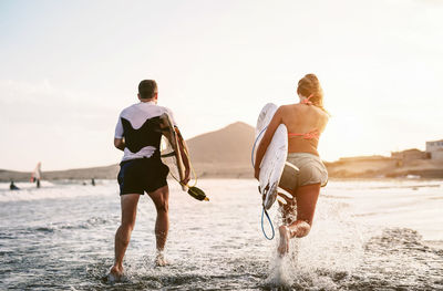 Rear view of couple running on beach against sky