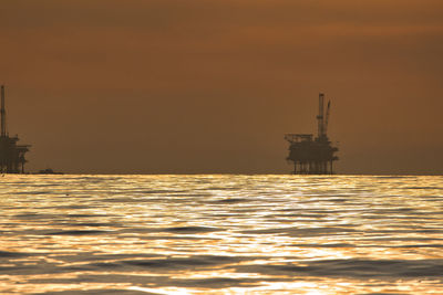 Silhouette built structure by sea against sky during sunset