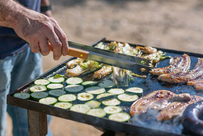 Hand of a person cooking different meats and vegetables on a barbecue